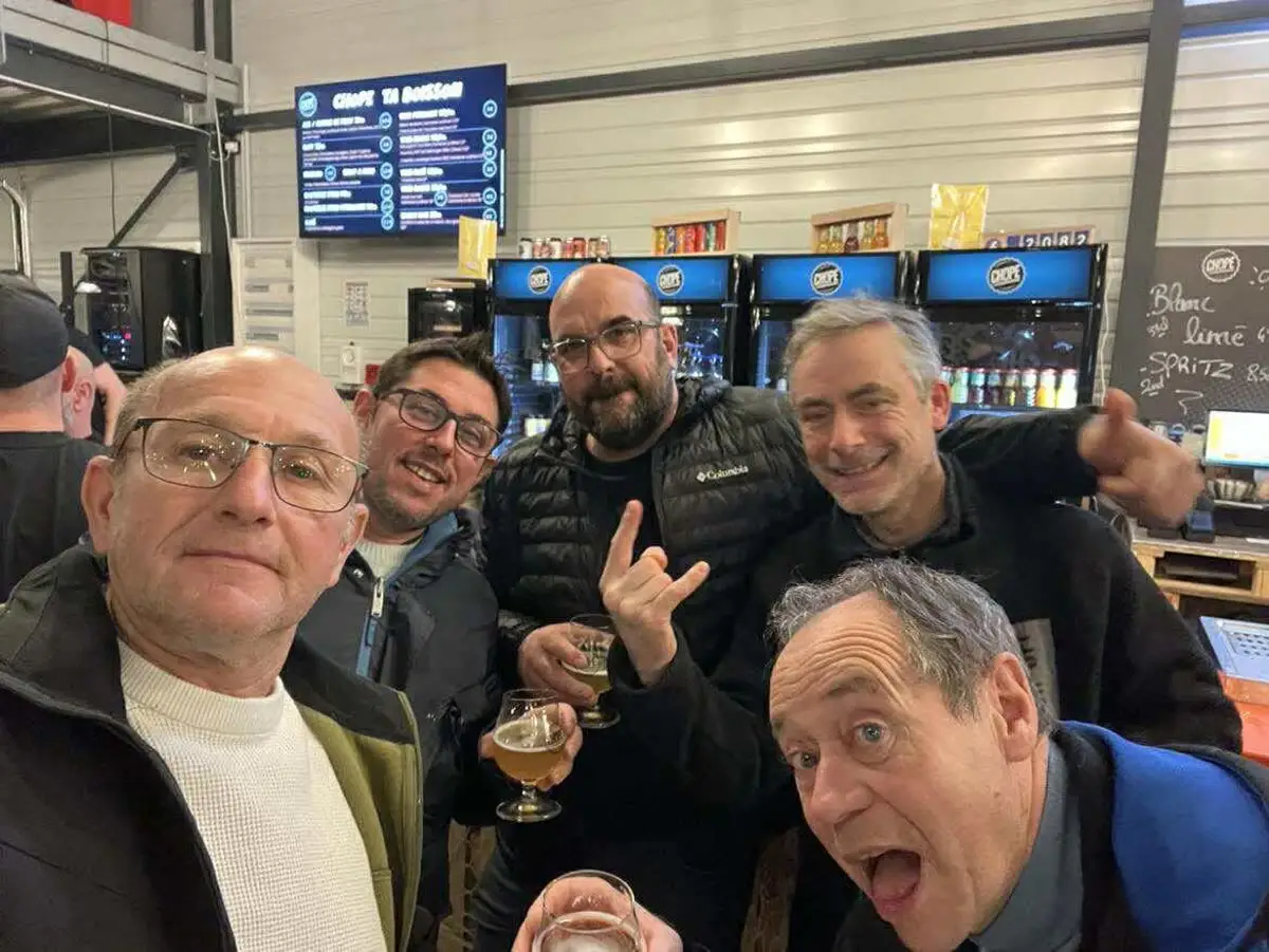 Cinq membres du club réunis au bar après une rencontre, verres à la main.