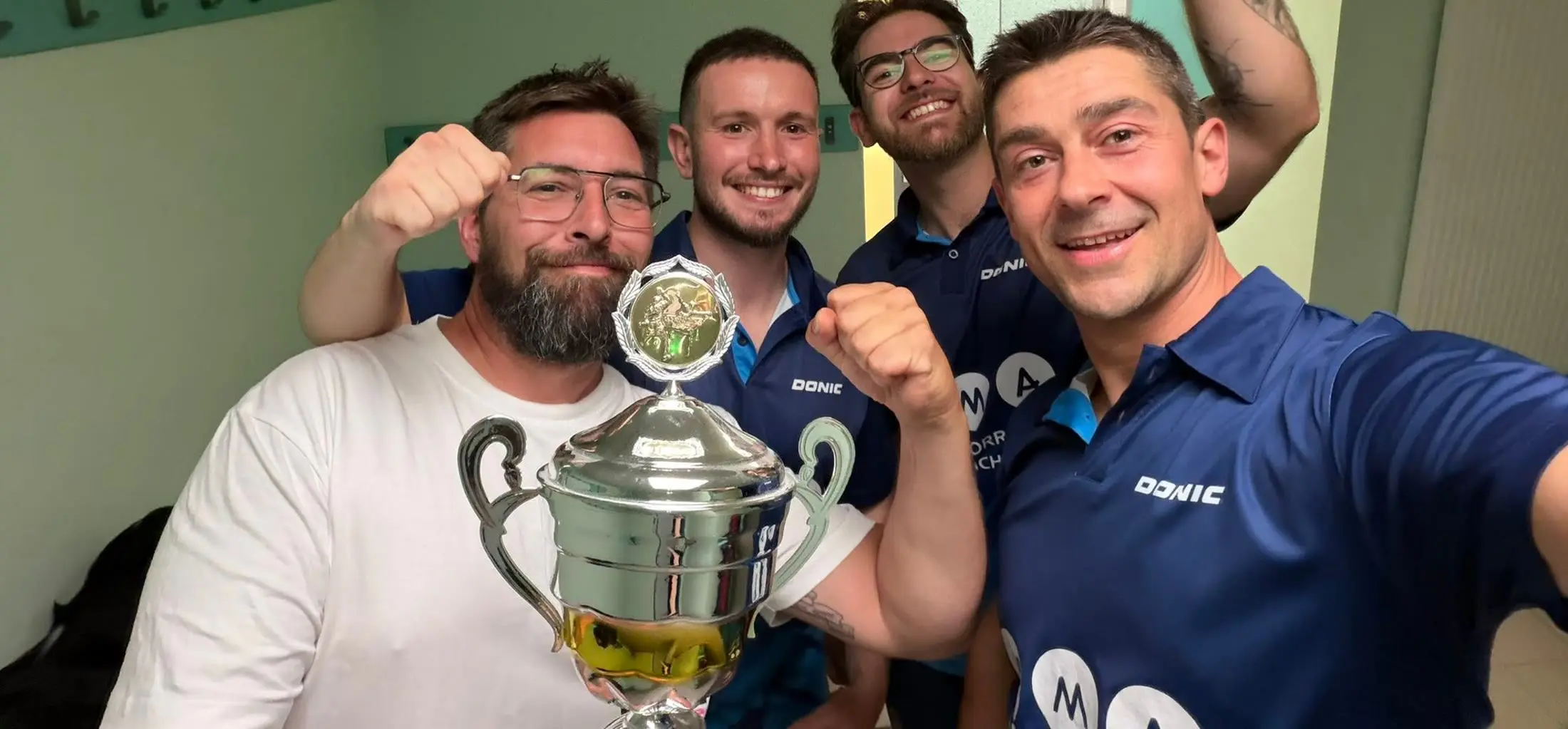 Quatre joueurs du club serrant le poing autour d'une coupe remportée en championnat.